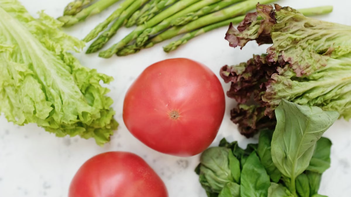 Top view of fresh asparagus, lettuce, basil, and tomatoes, highlighting healthy and nutritious ingredients.